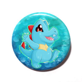 A cute chibi version of Totodile from Pokemon drawn by Camie M. Anderson on a handmade button.